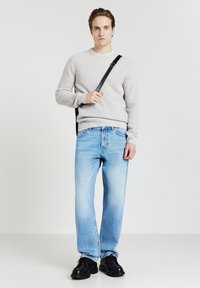Hellgrauer, strukturierter Pullover mit langen Ärmeln, kombiniert mit hellblauen, geraden Jeans. Schwarze Schuhe und eine schwarze Schultertasche runden den Look ab.