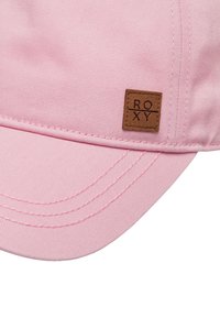Gorra de béisbol de color rosa claro, hecha de algodón texturizado, con visera curvada y una etiqueta de cuero marrón con "ROXY" grabado.