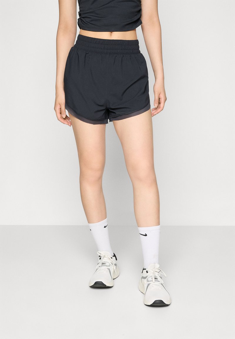 Calções desportivos pretos com uma cintura elástica, apresentando um corte descontraído e bainha em contraste. Combinados com meias brancas e sapatilhas.