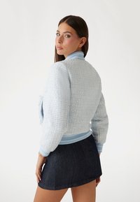 Giacca bomber in tweed azzurro chiaro con polsini e orlo a coste. Presenta un motivo tessuto e testurizzato. Abbinata a una gonna in denim scuro.
