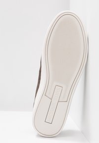 Hnědá texturovaná bota s bílou podrážkou, vybavená gumovou spodní částí a vyraženým logem "Michael Kors" na boku.