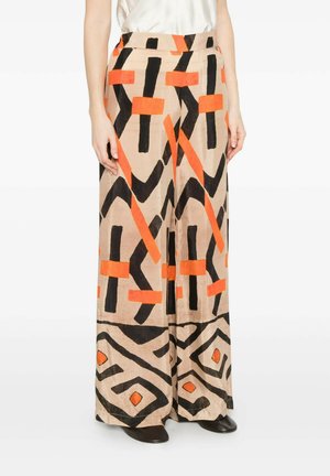 Pantaloni beige a gamba larga con motivi geometrici astratti neri e arancioni, indossati con un top bianco e scarpe nere.