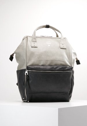 Szary i czarny plecak z górnymi uchwytami, przednią kieszenią na zamek błyskawiczny oraz bocznymi paskami, prezentowany na białym piedestale na jednolitym tle.