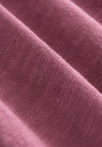 Texturiertem Stoff in einem sanften Rosaton, der feine Strickdetails und eine glatte Oberfläche mit subtilen Farbvariationen zeigt.