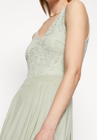 Ljusgrön klänning med V-ringning, med en spetsöverdel och en svängande kjol. Tyget är mjukt med en lätt glans.