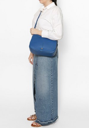 Sac bandoulière en cuir bleu avec une forme arrondie, surface texturée, une sangle réglable unique et un détail en métal doré simple.