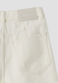 Krémové džíny z denimové látky s texturovaným povrchem, které mají výraznou zadní kapsu a obdélníkovou nášivku s logem na pase.