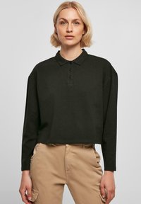 Svart langermet polo-skjorte, kort design, knappestolpe, mykt materiale, har krage, kombinert med lyse bukser.