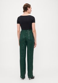 Must mustripsiga must topp ja rohelised sädelevad lai-püksid. Pükstel on läikiv, tekstuuriline pind ja need on sobitatud vöökohaga.