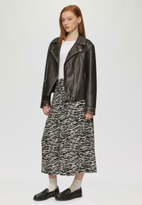 Zwarte leren motorjack met zilveren ritsen, gecombineerd met een gemusterde midirok in zwart en crèmekleur, en zwarte instapschoenen met dikke zolen.