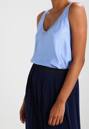 Light blue sleeveless blouse in smooth fabric with a V-neck and gathered detail, paired with a pleated dark navy skirt featuring an elastic waistband.