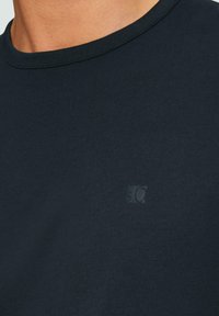 T-shirt in cotone blu navy con colletto rotondo, caratterizzato da un sottile logo in rilievo sul petto. Tessuto liscio, design semplice.