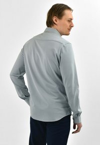 Lichtgrijs overhemd met lange mouwen, een puntkraag, knoopmanchetten, een gladde textuur en een ronde zoom; gedragen door een model dat zich van de camera afkeert.