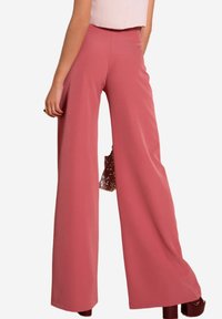 Pantalons évasés en tissu rose doux, avec une taille haute et un design fluide. Le matériau semble léger et lisse.