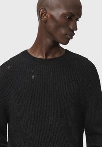 Suéter de punto negro con textura acanalada, que presenta pequeños agujeros. Cuello redondo y un corte holgado, que resalta la suavidad del material.