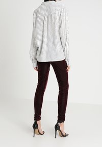 Vit skjorta med vita prickar och ryggrynk, kombinerad med vinröda sammetsleggings och svarta högklackade skor.