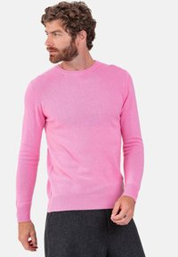 Pull rose à col rond en tissu tricoté doux avec manches longues et poignets côtelés. Porté avec un pantalon gris texturé. Finition lisse.