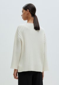 Cream-colored ribbed sweater with a relaxed fit, featuring wide sleeves and a side slit for added texture and comfort.
