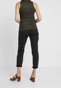 Tmavě modré slim-fit džíny v kombinaci s ribbed olivově zeleným tílkem. Hnědé sandály na podpatku s krokodýlím vzorem dokončují celkový vzhled.