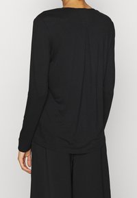 Maglietta nera a maniche lunghe con una consistenza morbida, scollatura rotonda e dettagli di cucitura sottili sul retro. Ideale per un look informale.