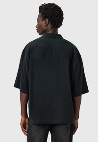 Chemise noire à manches courtes avec une coupe ample et un col classique. Présente un ourlet droit et une texture lisse, sur fond gris.