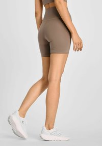 Brązowe, wysokie szorty z dopasowanym krojem, gładką teksturą i długością do kolan, zestawione z białymi butami sportowymi.