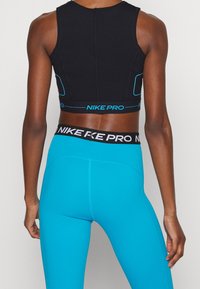 Zwarte sportbeha met blauwe accenten en branding; gecombineerd met hooggesneden, nauwsluitende turquoise legging. Gladde, rekbare stof.