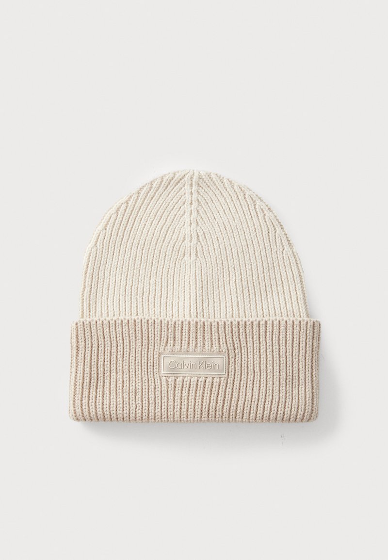 Beige gestrickte Mütze mit umgeschlagenem Rippenbund, die ein strukturiertes Muster und ein Schild mit "Calvin Klein" auf einem rechteckigen Patch aufweist.