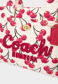 Sac fourre-tout en toile avec motif cerise rouge, texte brodé rouge "Coach New York" et fermoir à tour doré avec étiquette en cuir rouge.