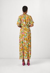 Blomster maxi kjole med korte ærmer, orange og grøn baggrund, prydet med lyserøde og blå blomster, taljebånd og højhælede lyserøde sandaler.