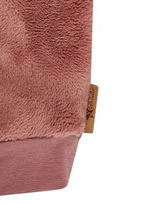 Weicher, staubig rosa Fleece-Stoff mit einem strukturierten Strickbündchen und einem kleinen braunen Etikett, das in die Naht auf der rechten Seite genäht ist.