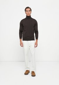 Dark brown turtleneck sweater, fitted design, ribbed cuffs and hem, paired with white pants and light brown suede shoes. Simple, clean lines.
