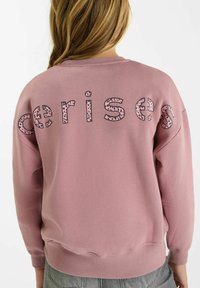Roze sweatshirt met een losse pasvorm, voorzien van een gestructureerde "cerises" print in zwart en een roze luipaardpatroon op de rug. Geribbelde manchetten en zoom.