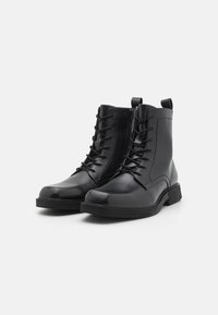 Bottes chevilles en cuir noir avec lacets à l'avant, fermeture éclair sur le côté, bout rond et semelle en caoutchouc texturée, avec des accents cousus sur le corps.