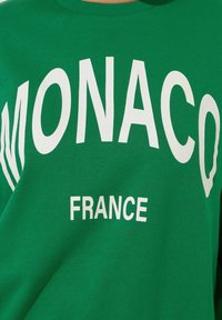 Zielona bluzka z białym napisem "MONACO" i "FRANCJA". Posiada ściągacz przy dekolcie i miękką fakturę materiału.