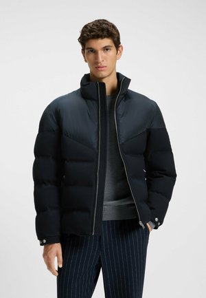 Navy puffer jacket with a high collar, contrasting shoulder panels, and front zip. Features buttoned cuffs and a smooth texture.