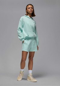 Mintgrön sweatshirt med huva och shorts, tillverkad av mjukt material, med en framfick, ribbade mudd och matchande sneakers.