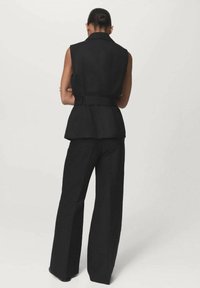 Chaleco negro sin mangas con una cintura ceñida y silueta de peplum, combinado con pantalones de pierna ancha, ambos hechos de tejido estructurado.