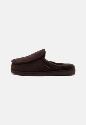 Brauner Slip-On-Hausschuh mit weichem Pelzfutter und kleinem Seitenlabel mit der Aufschrift „Shepherd“, seitlich vor einfarbigem Hintergrund dargestellt.