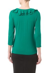 Grön långärmad topp med en volangkantad halsringning, gjord av ett mjukt tyg. Bakstycket är enkelt med en figursydd design och midjelång klippning.