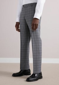 Pantalons gris à carreaux avec un motif de check subtil, coupe ajustée et design à devant plat. Associés à des chaussures en cuir noires et une chemise blanche.