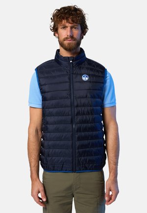 Gilet imbottito navy con design a righe orizzontali, zip frontale, colletto alto e logo sul lato sinistro del petto. Indossato sopra una camicia azzurro chiaro.