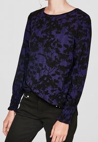 Blusa a maniche lunghe con un motivo floreale viola e nero, realizzata in tessuto leggero con polsini arricciati e scollatura rotonda.
