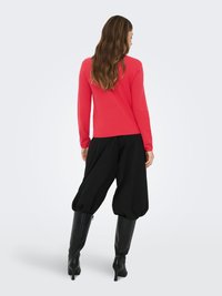 Czerwony top z długim rękawem zestawiony z czarnymi spodniami z obniżonym krokiem i czarnymi kozakami za kolano, prezentujący dopasowany krój i gładkie faktury.