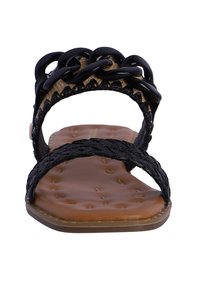 Sandalias trenzadas negras con parte superior de tejido, que presentan un detalle de cadena gruesa. La plantilla es marrón y acolchada, con una suela plana.