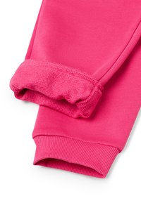 Světlé růžov�é tepláky s elastickými manžetami, jeden nohavice vyhrnutá, aby ukázala měkkou, strukturovanou podšívku.