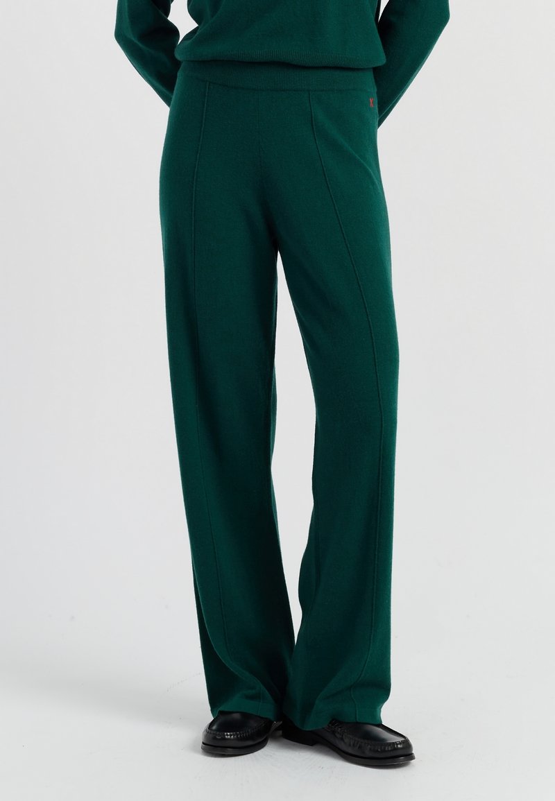 Groene wijde broek van zacht materiaal, met een hoge taille, zijnaad met stikselDetails en gecombineerd met zwarte instappers.