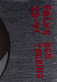 Grauene Socke mit roten gestrickten Text "FALKE BC5 35-41 TOURING." Das Material hat eine glatte Textur und ein dezentes Strickmuster.