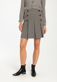 Zwart-witte houndstooth geplooide rok met dubbele knoopdetail, gedragen met zwarte enkellaarsjes. Geknoopte blouse voegt een patrooncontrast toe.