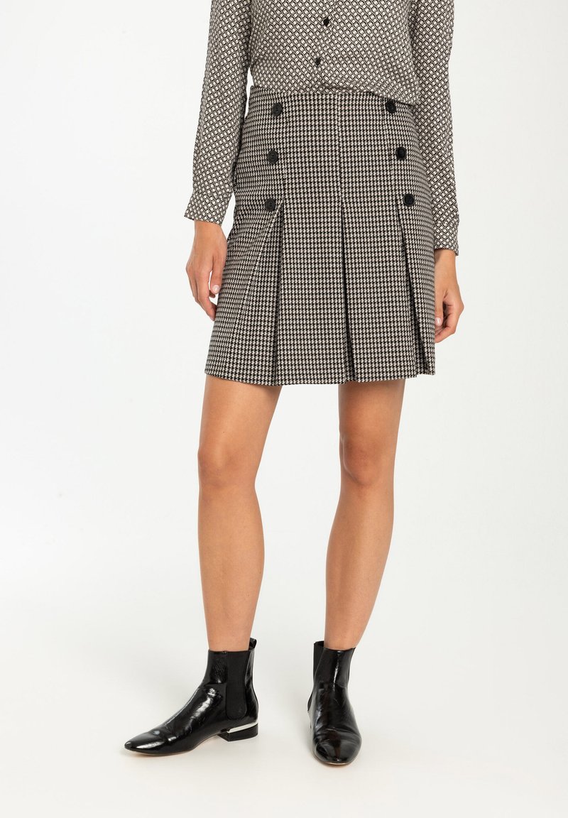 Zwart-witte houndstooth geplooide rok met dubbele knoopdetail, gedragen met zwarte enkellaarsjes. Geknoopte blouse voegt een patrooncontrast toe.